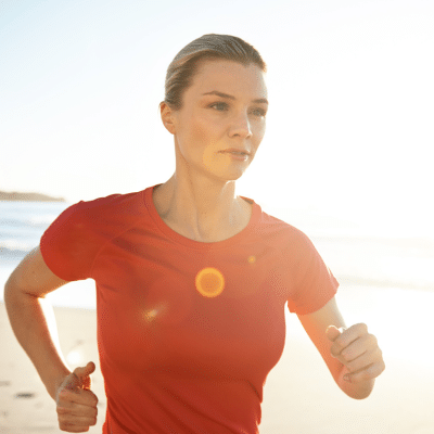 Woman running along a beach with sun shining bright, representing medical weight loss program, beyond prescriptions