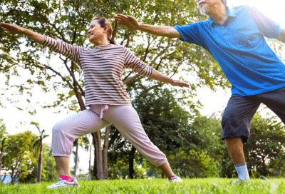Older people doing stretching yoga exercises outside in a park, representing weight loss programs