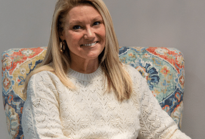 Woman smiling, sitting on a colorful chair at the weigh station, representing how to get past a weight loss plateau