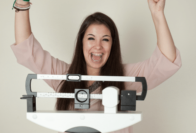 Woman celebrating weight loss milestones on the scales with her hands up in the air